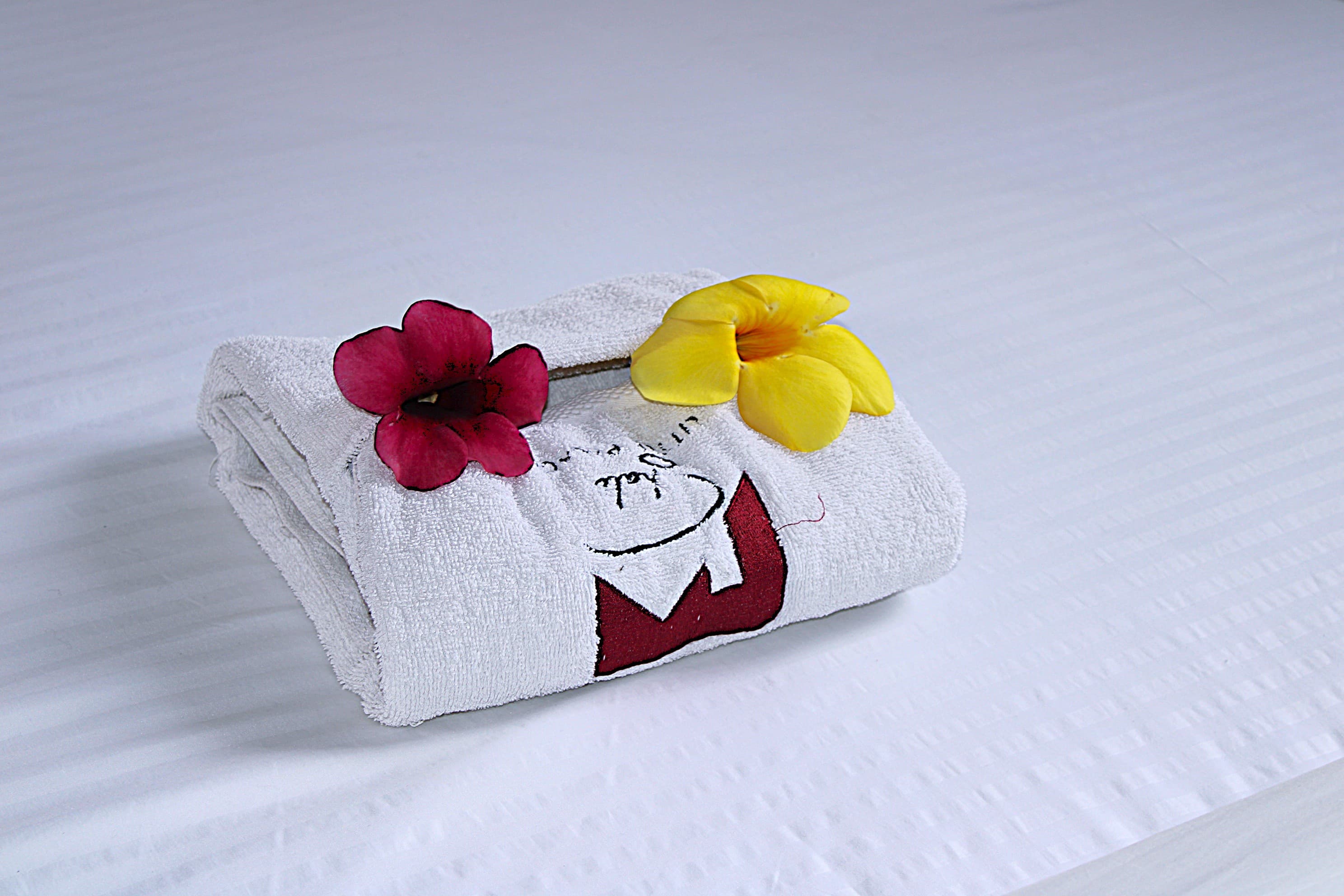 A folded towel and fresh flowers laid on white bed linen